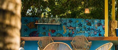 A poolside area with wicker chairs, a tiled wall with fish illustrations, and hanging lights.