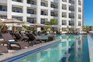 Una piscina al aire libre, sombrillas, sillones reclinables de piscina