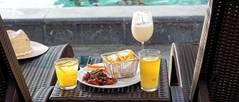 A poolside setting with lounge chairs, a table with a drink and snacks, and a pool in the background.
