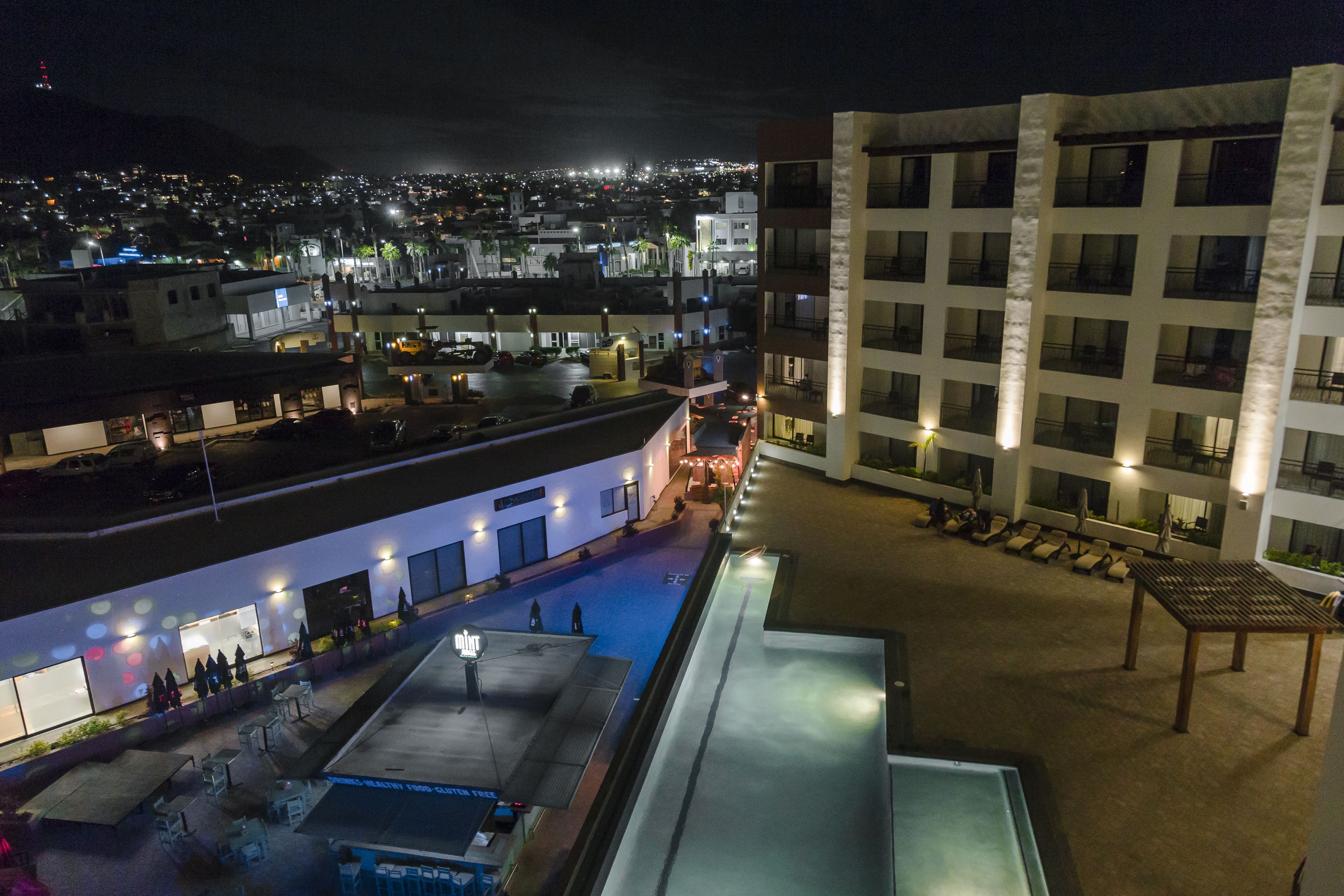 Una terraza en la azotea con mobiliario exterior, piscina y vistas a un paisaje urbano nocturno.