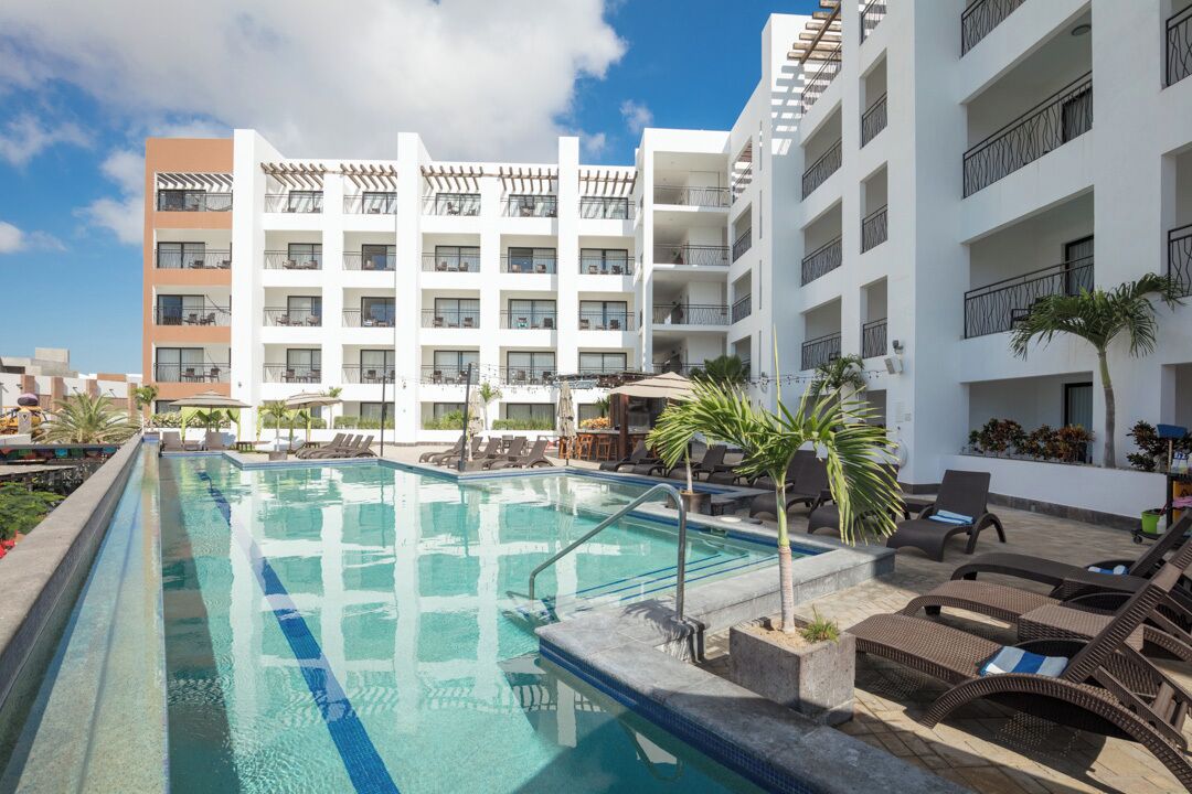 A pool area with lounge chairs and a building with multiple balconies.