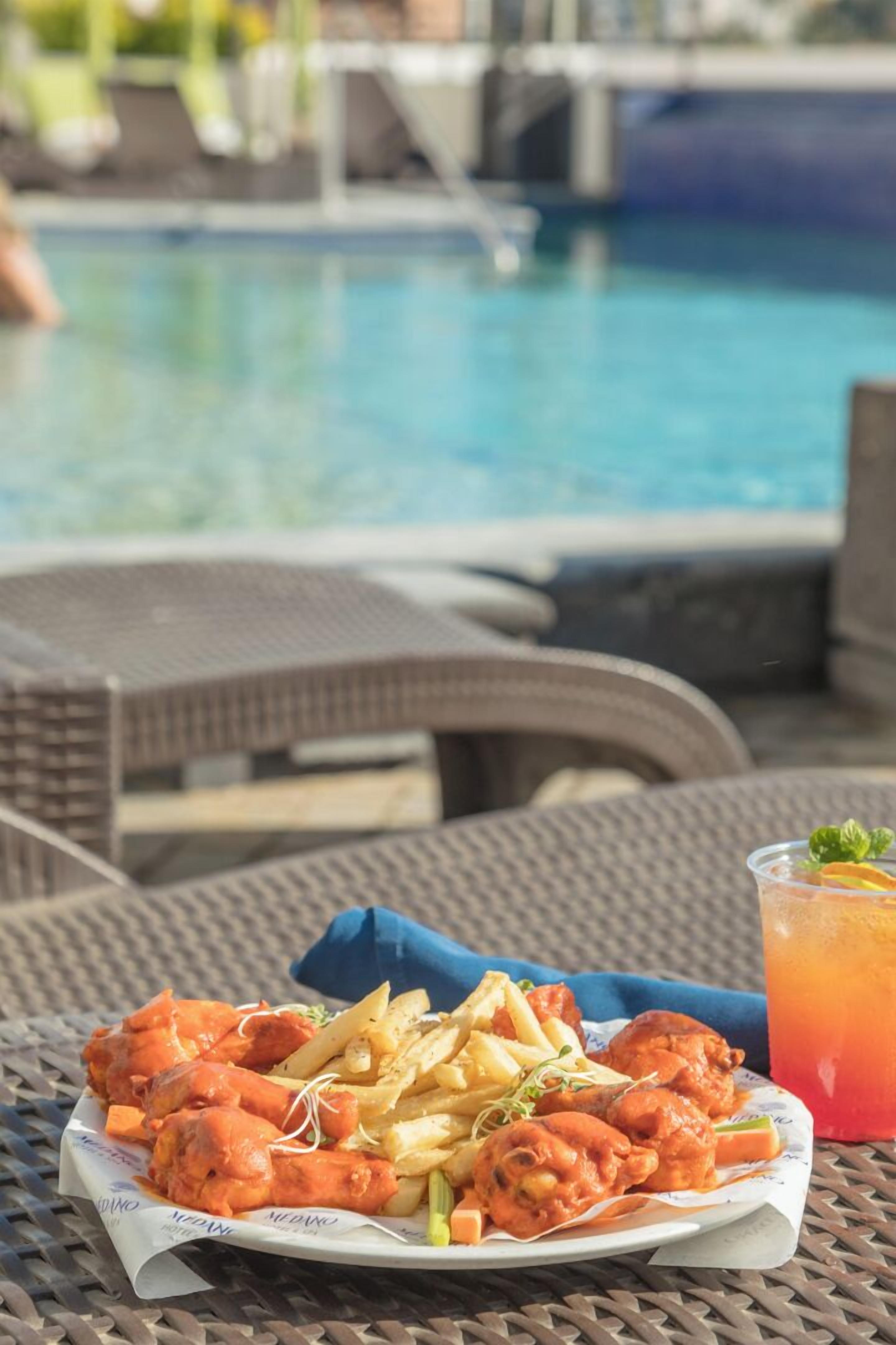 A dining table with a plate of food and a drink, near a poolside area.