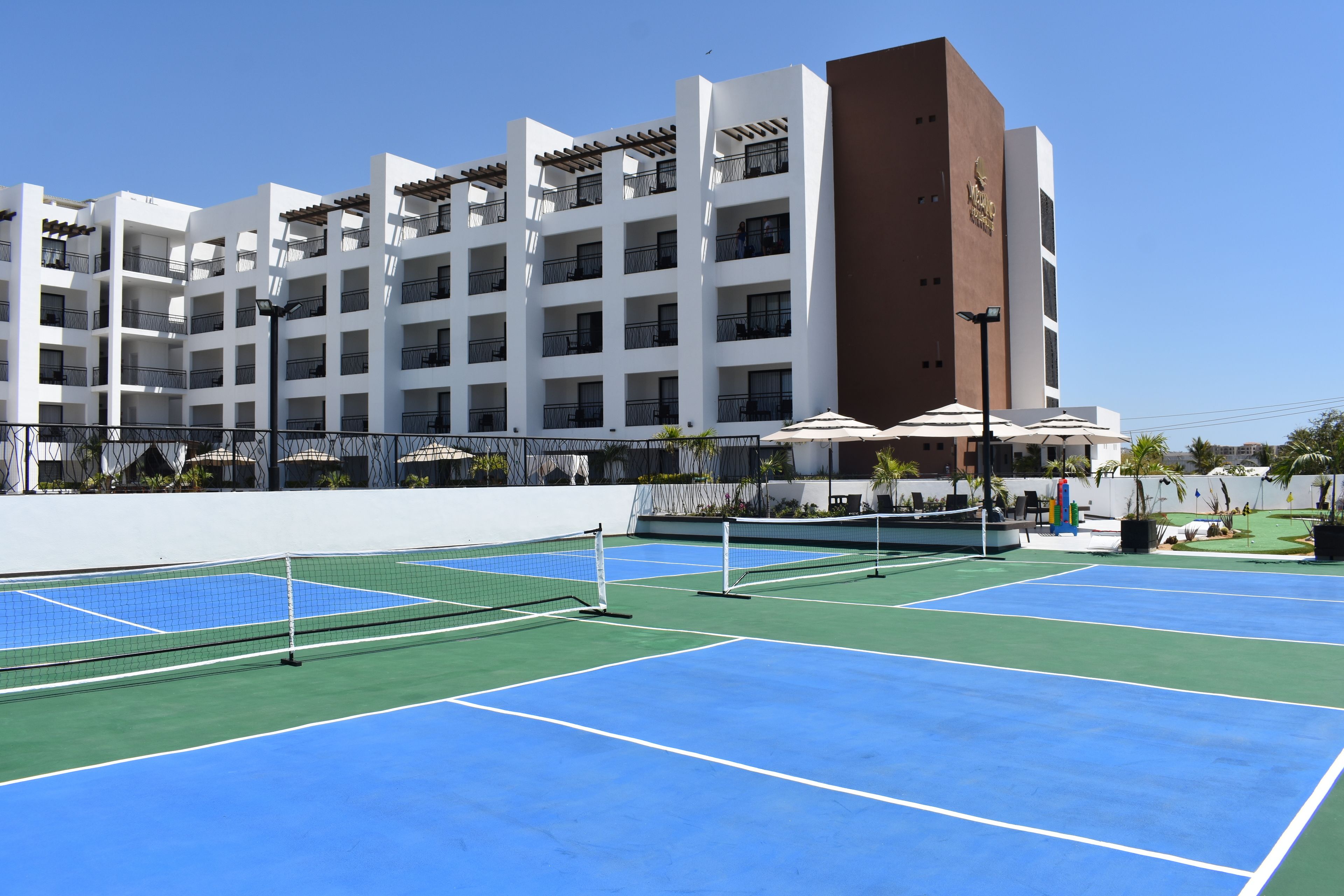 A multi-story hotel with a tennis court in the foreground.