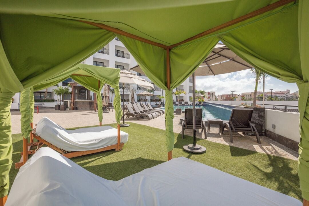 Un área de piscina en la azotea con una cama, sillas de descanso y sombrillas.