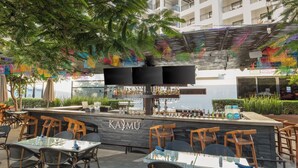 An outdoor bar area with a counter, seating, and a view of a building in the background. - Medano Hotel and Spa (Cabo San Lucas)
