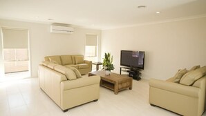 Un soggiorno moderno con due divani beige, un tavolino in legno e un televisore a schermo piatto.