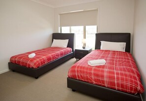 A hotel room with two beds, each with red bedding and white pillows, and a small bedside table with a lamp. - Villa Saltwater (POINT COOK)