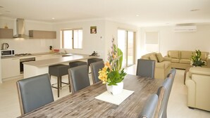 Una cucina moderna con isola centrale, zona pranzo con tavolo e sedie in legno, e soggiorno con divano beige.