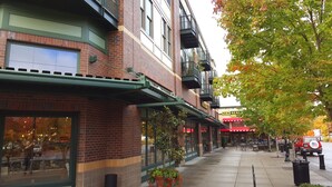 A brick building with a green awning, outdoor seating, and a storefront with a sign that reads "NEW SEASON." - Orenco Lofts (Hillsboro)