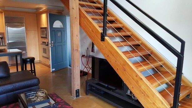 A modern kitchen with built-in appliances, a wooden staircase, and a cozy seating area with a television. - Orenco Lofts (Hillsboro)
