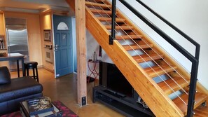 Una cocina moderna con electrodomésticos integrados, una escalera de madera y una zona de estar acogedora con televisión.