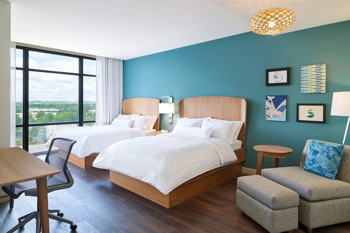 Une chambre d’hôtel avec deux lits, un bureau, une chaise et une vue sur la ville.