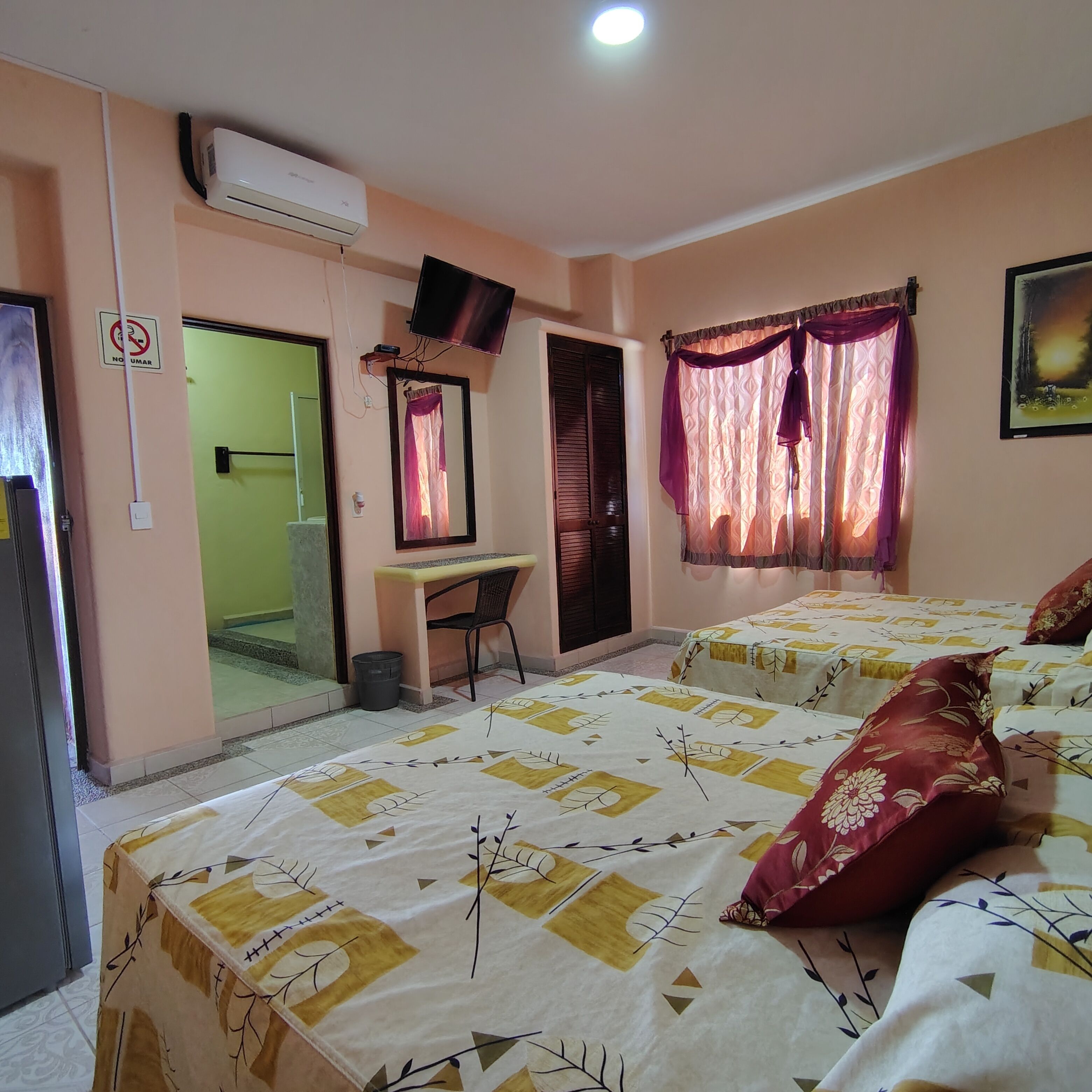 A hotel room with two beds, a desk, a chair, a TV, and a window with curtains.