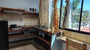 Una cocina con estufa a gas, microondas, fregadero y una ventana con cortinas.