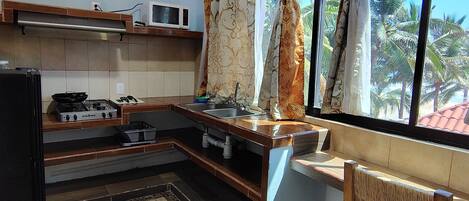 Una cocina con estufa a gas, microondas, fregadero y una ventana con cortinas.