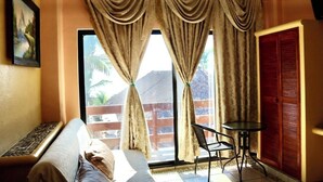 Una habitación con cama, una mesita, una silla, una ventana con cortinas y una puerta.