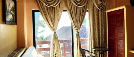 A room with a bed, a small table, and a chair, a window with curtains, and a door.