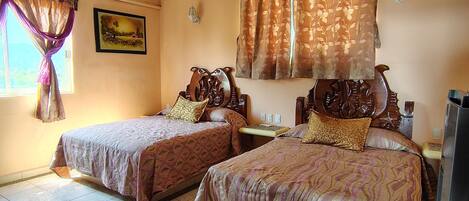 A hotel room with two beds, a window with curtains, a wall-mounted lamp, and a framed picture.