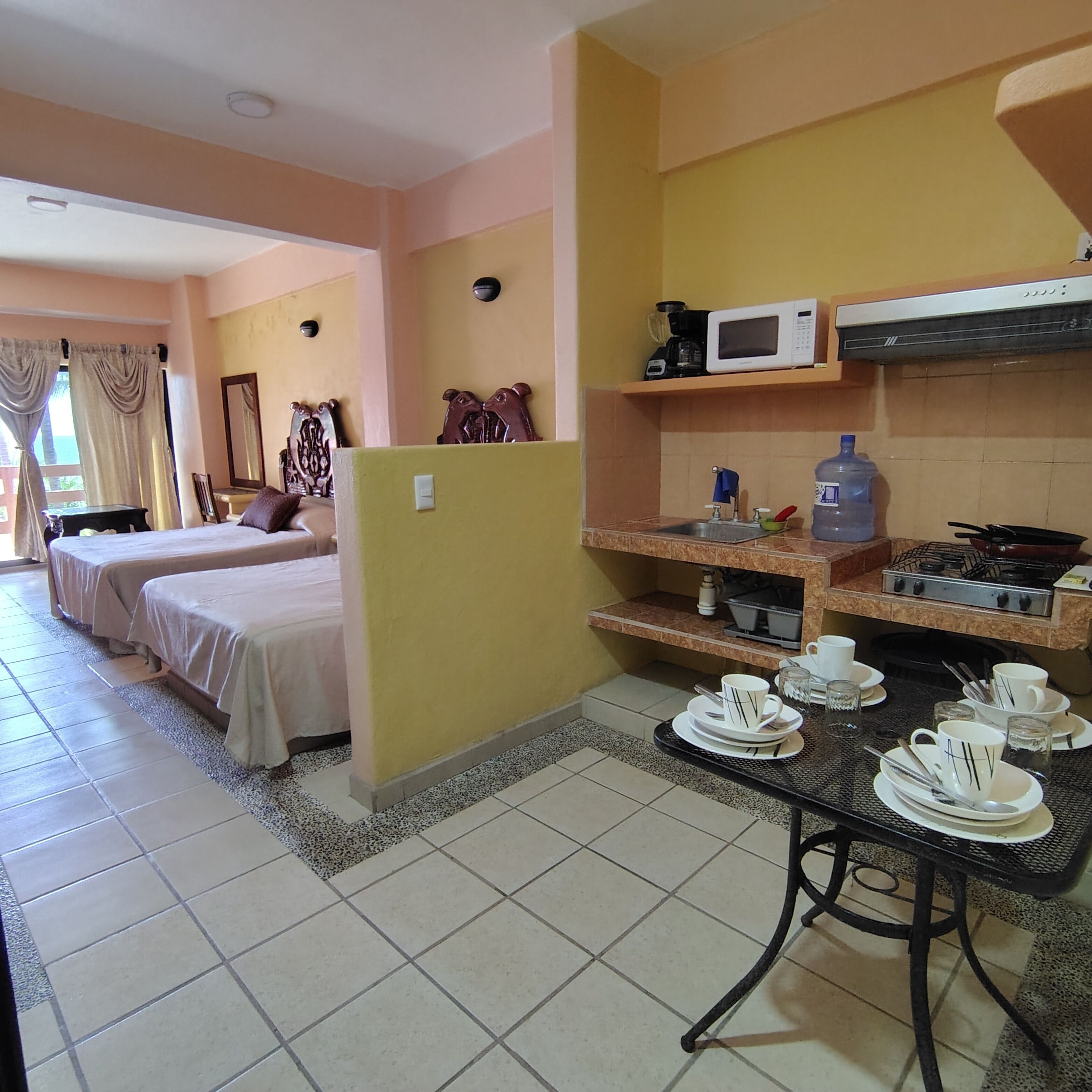 Habitación de hotel con dos camas, una kitchenette y un comedor con vajilla.