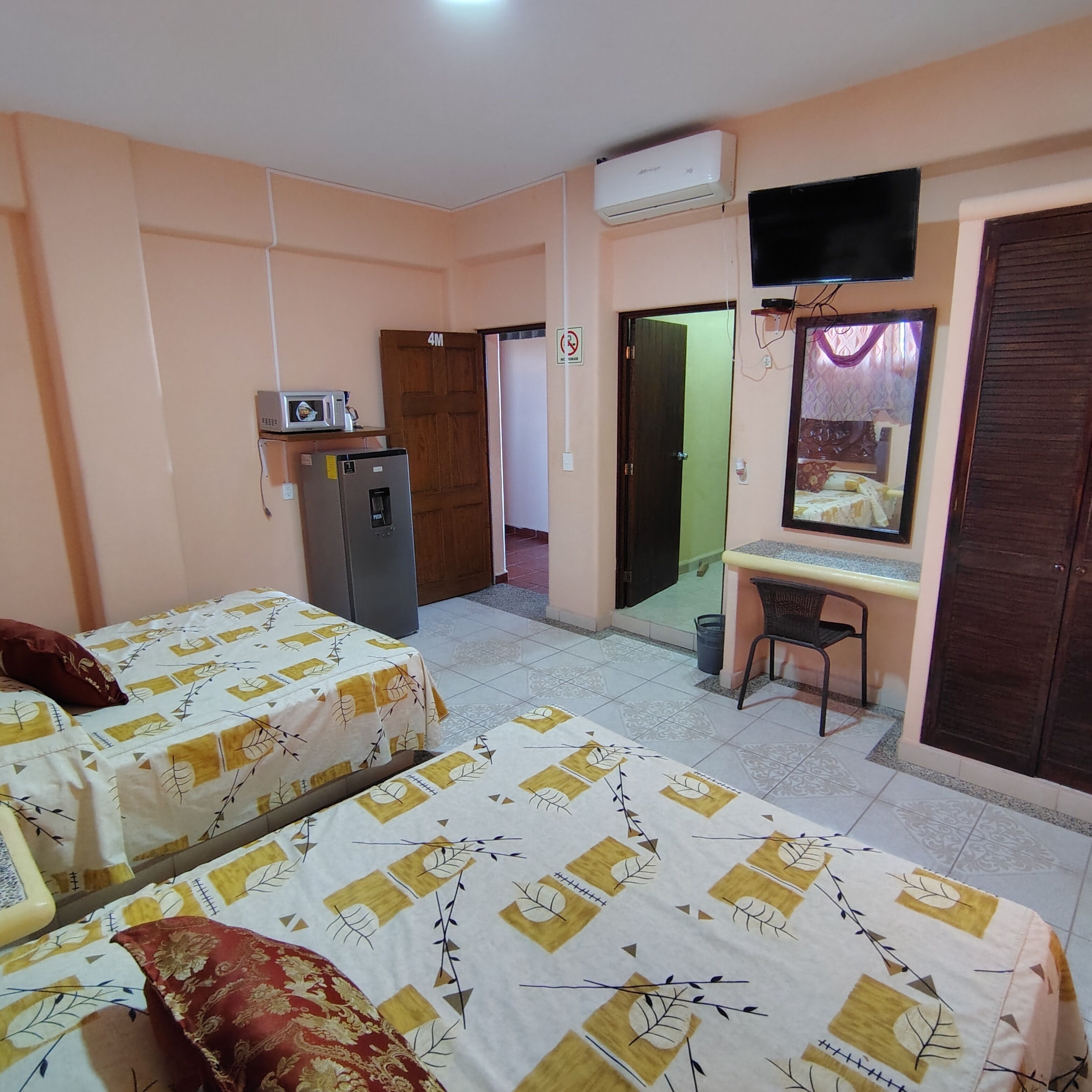A room with two beds, a desk, a television, and an air conditioning unit.
