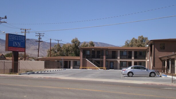 A two-story motel with a parking lot and a mountain in the background.