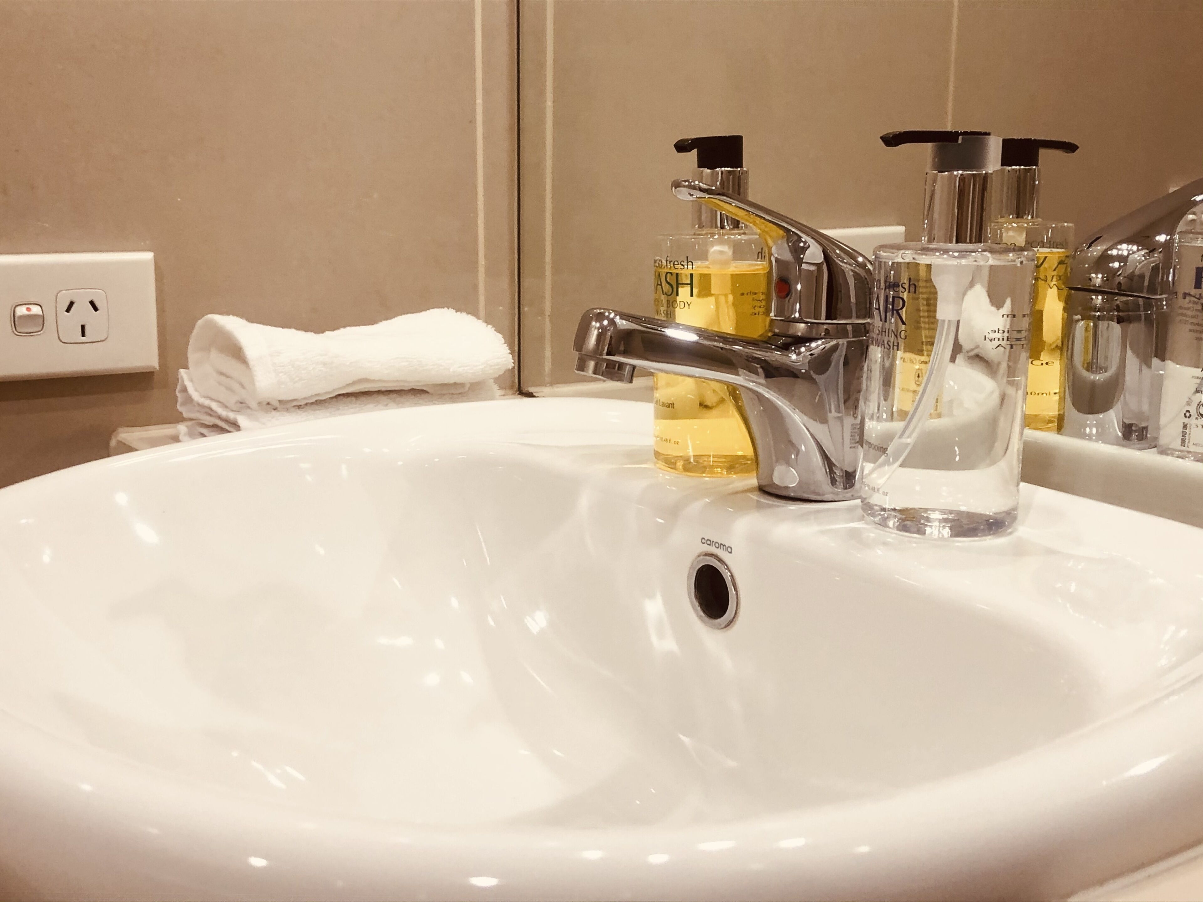 A white bathroom sink with a chrome faucet, two soap dispensers, and a white towel on a rack.