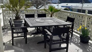 A terrace with a table and chairs, potted plants, and a view of the sea and mountains.