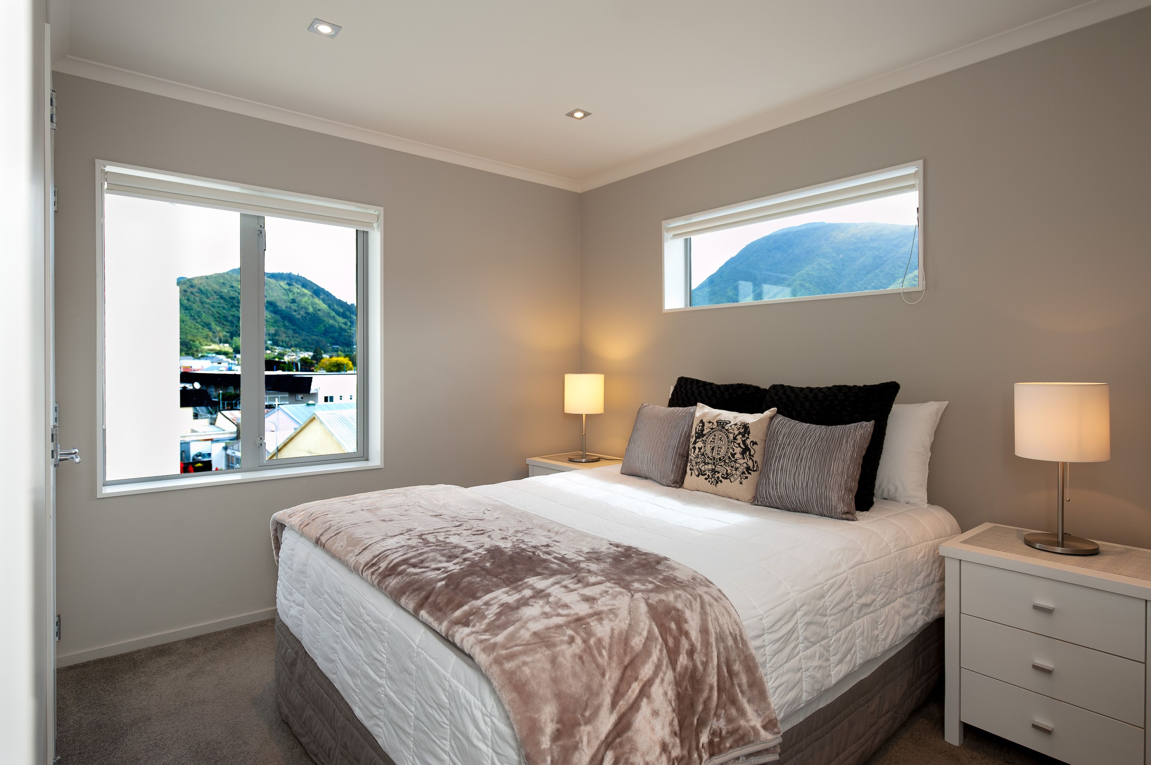 A bedroom with a large bed, two bedside tables with lamps, a window with a mountain view, and a door.