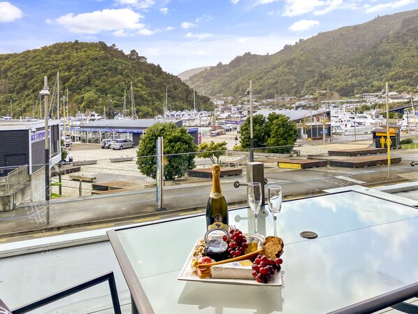 A table with a bottle of champagne, glasses, and a cheese platter with grapes and crackers. - Picton Waterfront Apartments (Picton)