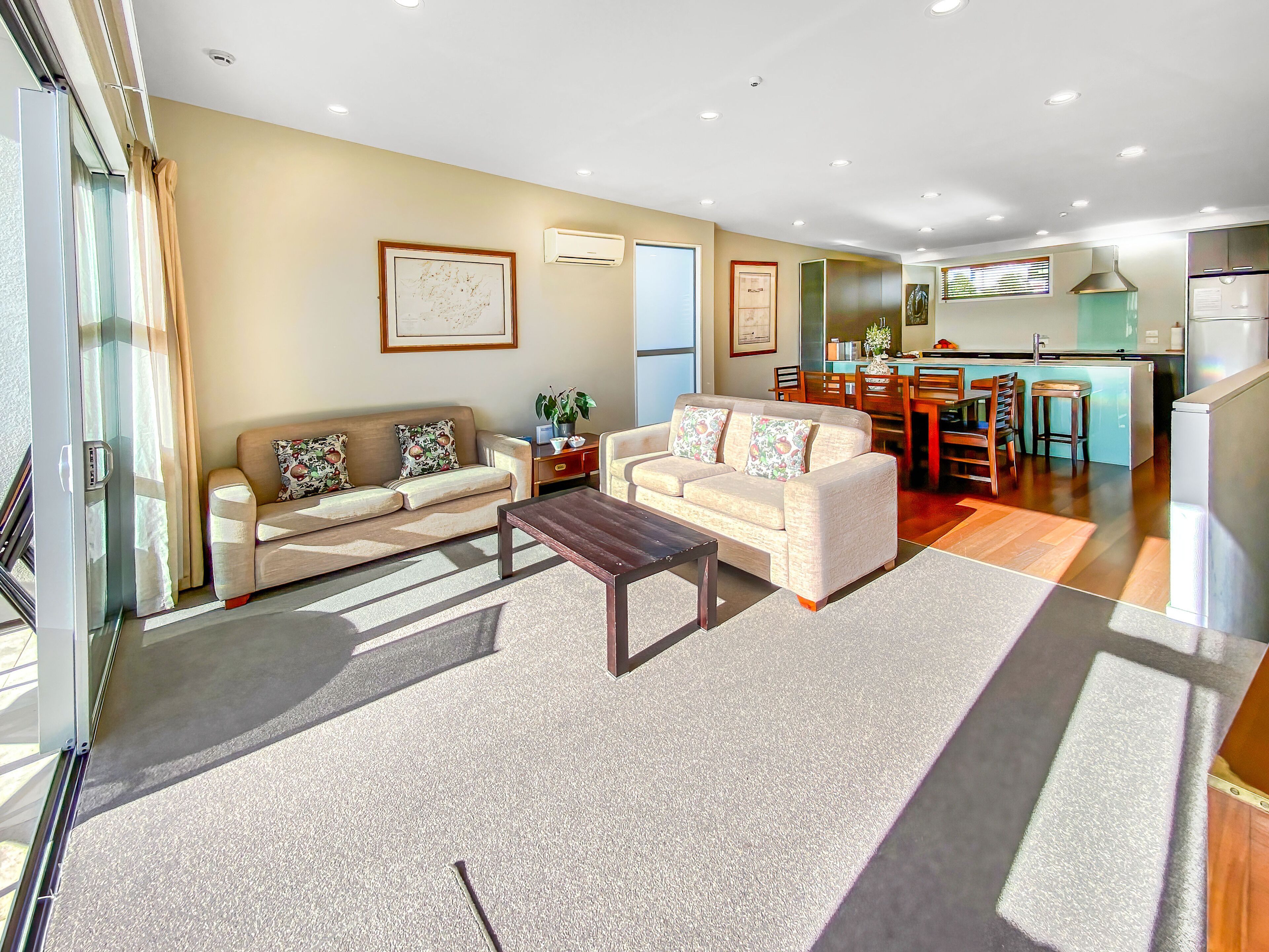 A modern living room with a sofa, coffee table, and a dining area with chairs and a kitchen in the background.