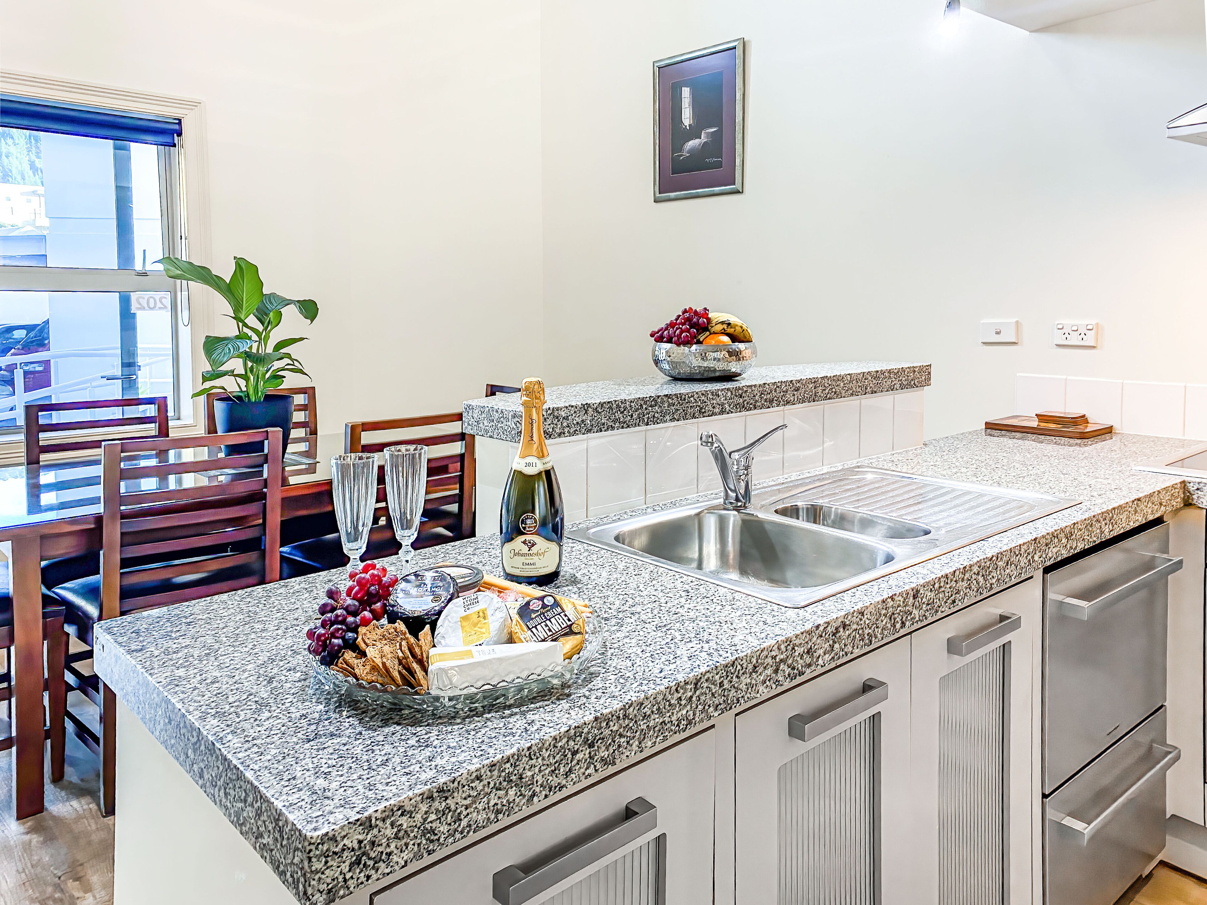 A modern kitchen with granite countertops, stainless steel appliances, and a dining area with wooden chairs and a potted plant.