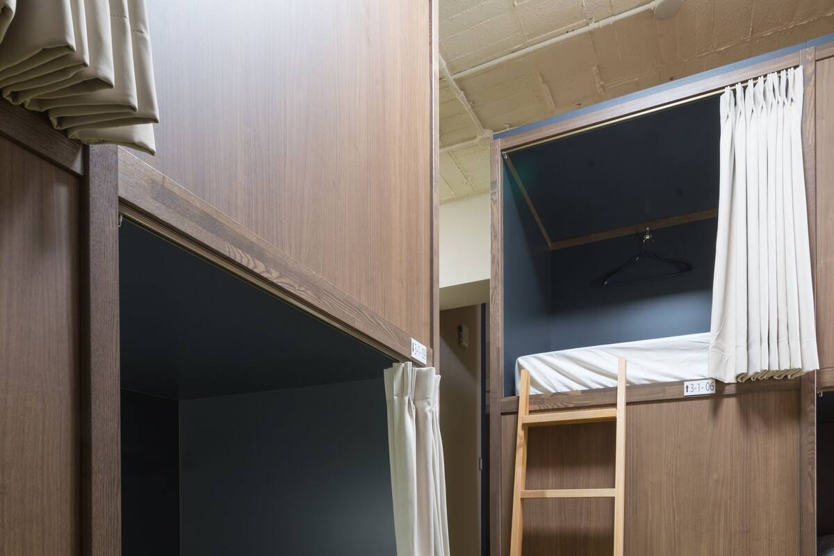 A dormitory room with bunk beds, a wooden ladder, and a green carpet.