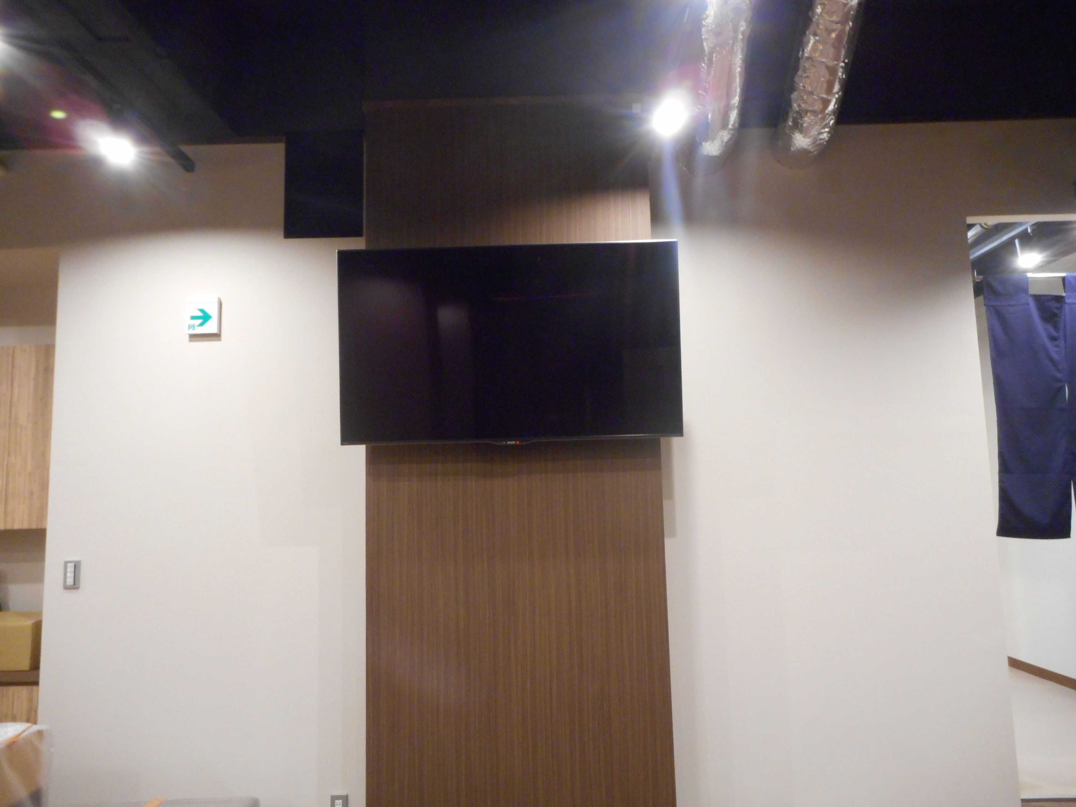 A room with a flat-screen TV mounted on the wall, a wooden panel, and a blue curtain.