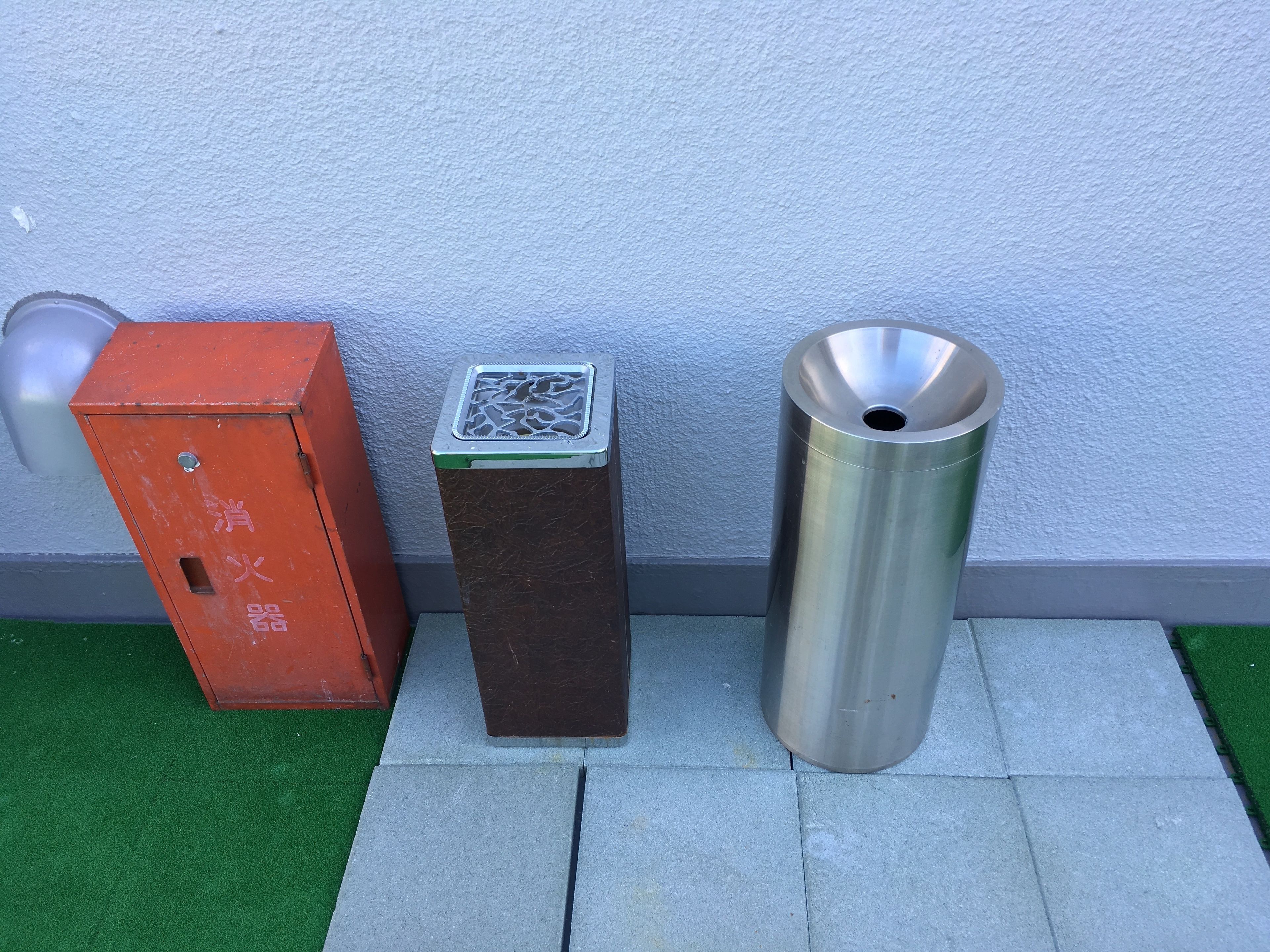 Three trash bins of different designs and colors against a wall with a textured surface.