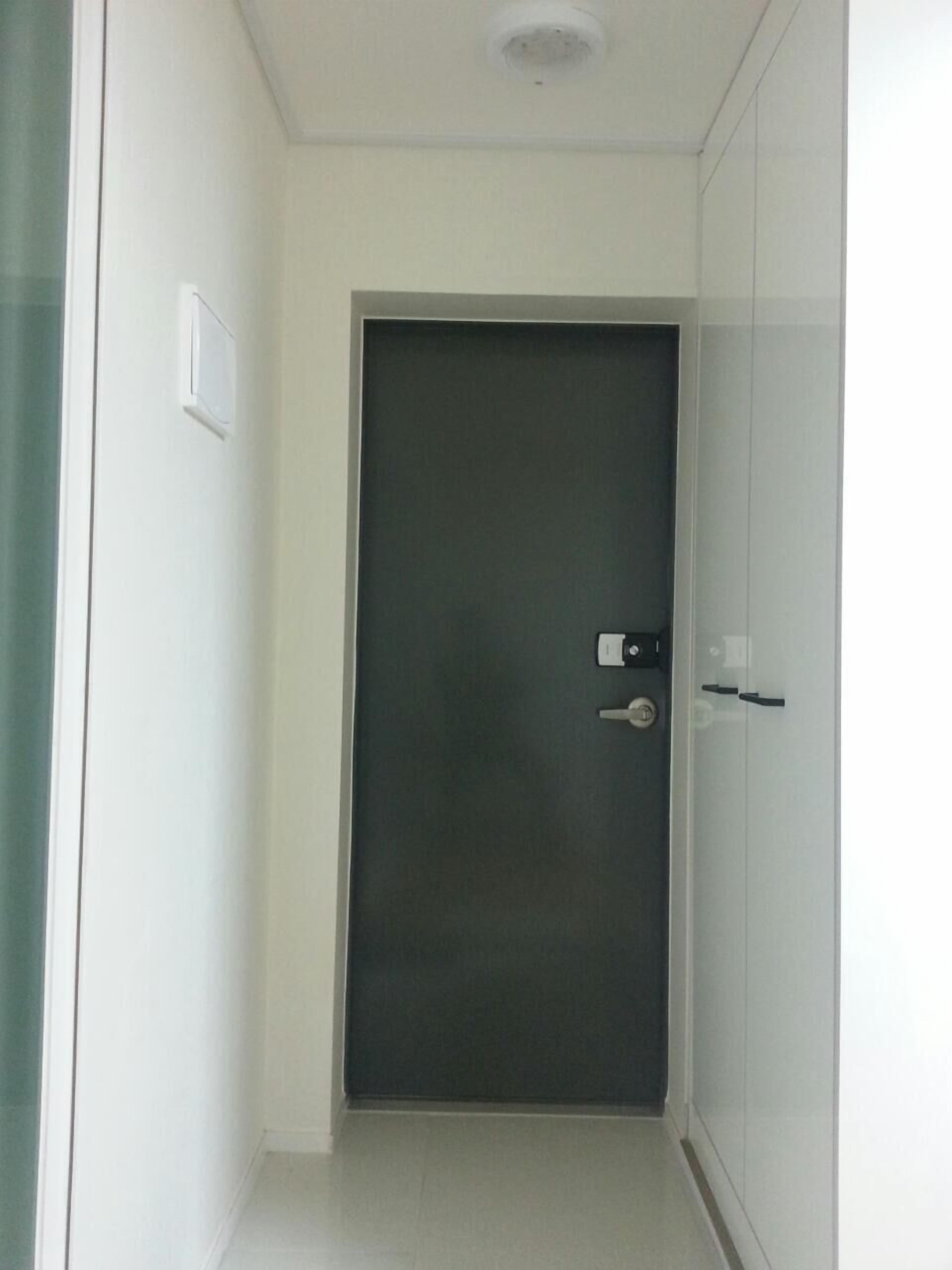 A narrow hallway with a dark door, a light switch on the wall, and a white door on the right.
