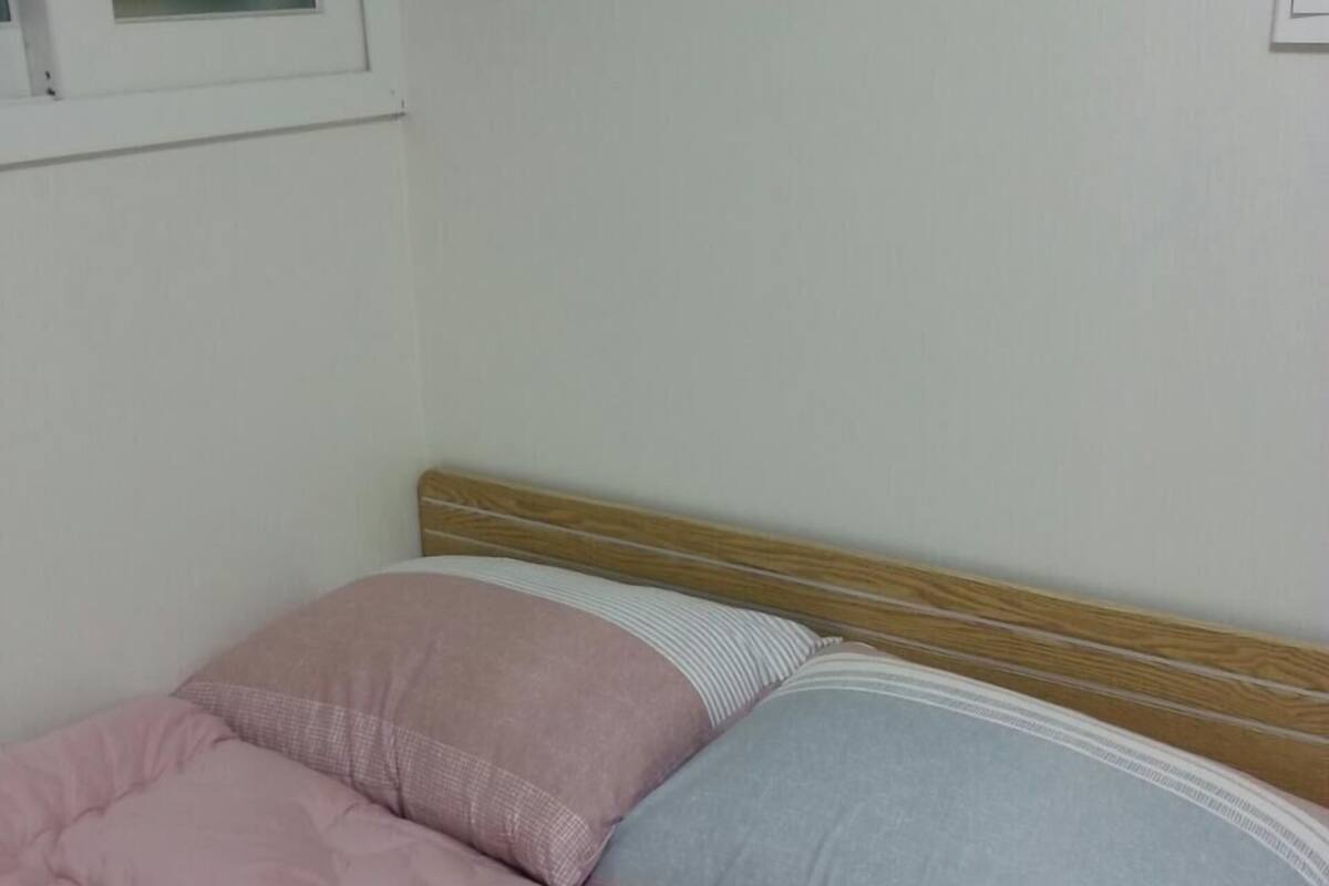 A bed with a wooden headboard, a pink and a blue pillow, and a striped blanket.