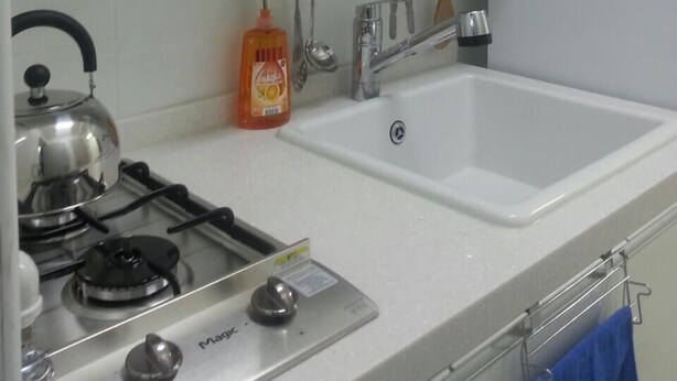 Uma cozinha com fogão a gás, chaleira, pia e um suporte para utensílios.