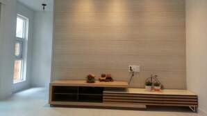 Uma sala de estar moderna com um aparador de madeira embutido, uma janela e uma pequena prateleira com objetos decorativos.