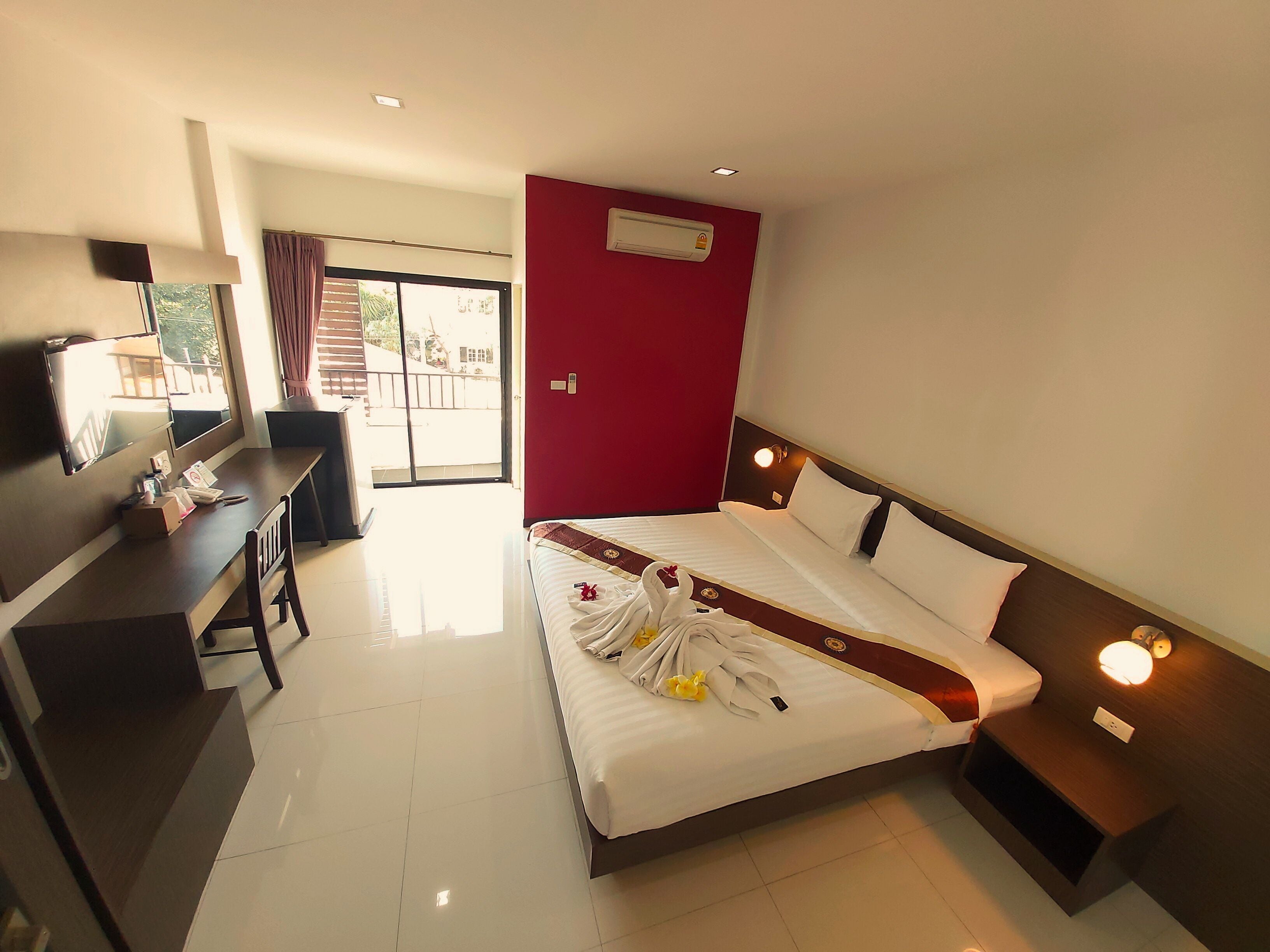 Une chambre d’hôtel avec un lit, un bureau, une chaise, une télévision et un mur rouge.