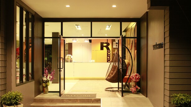 A hotel entrance with a reception desk, a 'Welcome' mat, and a '7-come' mat. - The Siri Place (Udon Thani)