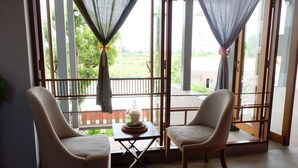 Een kamer met twee stoelen gericht op een balkon, een kleine tafel met een decoratief object, en uitzicht op groen.