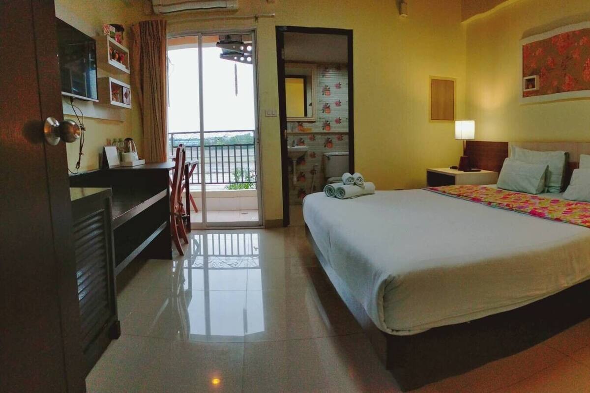 Habitación de hotel con cama, dos mesitas de noche, una lámpara, televisión, puerta al balcón y un cuadro floral en la pared.