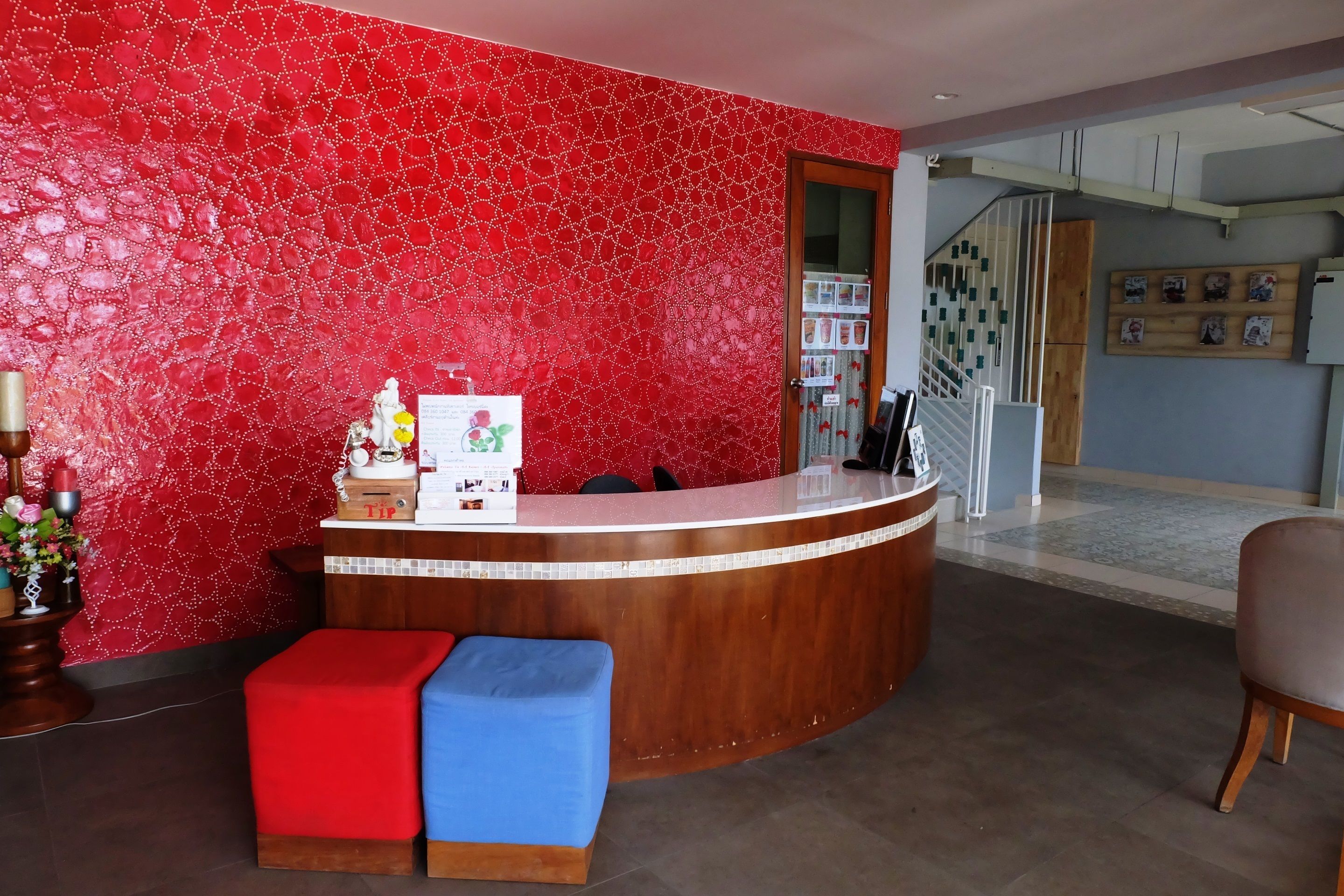 A reception area with a red patterned wall, a wooden reception desk, a blue and red bench, and a staircase in the background.