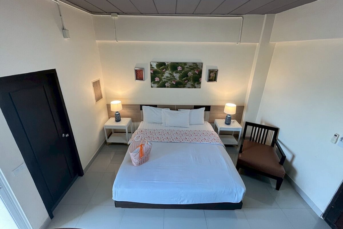 Habitación de hotel con una cama grande, dos mesitas de noche con lámparas, una silla, una puerta y una lámpara en el techo.