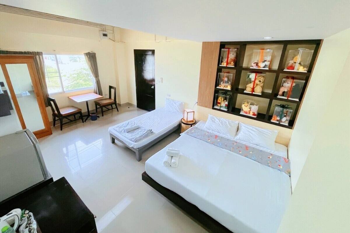 Habitación de hotel con dos camas individuales, una mesita con sillas, un escritorio y un estante con objetos decorativos.