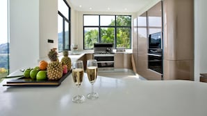 A modern kitchen with large windows, a dining table with fruit and champagne glasses, and built-in appliances.