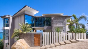 A modern house with large glass windows, a stone facade, and a view of the ocean.