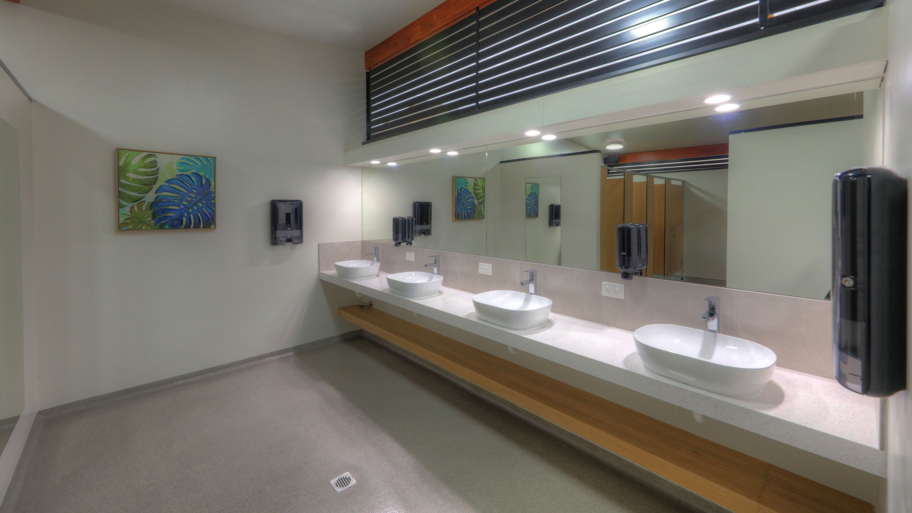 Un baño moderno con tres lavamanos, un espejo grande y obras de arte en las paredes.