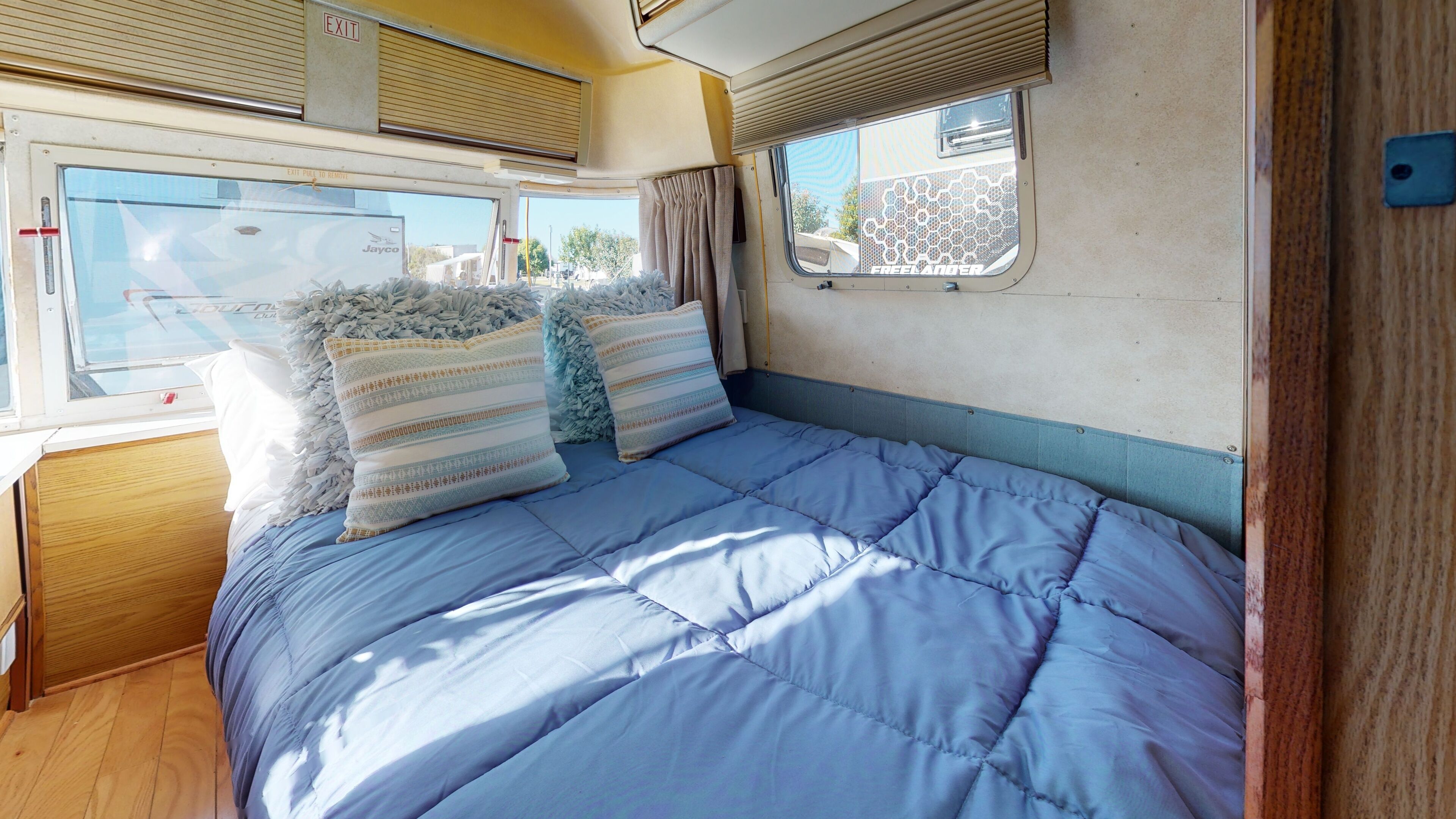 A compact RV interior with a bed, two pillows, and a window with a view of the outside.