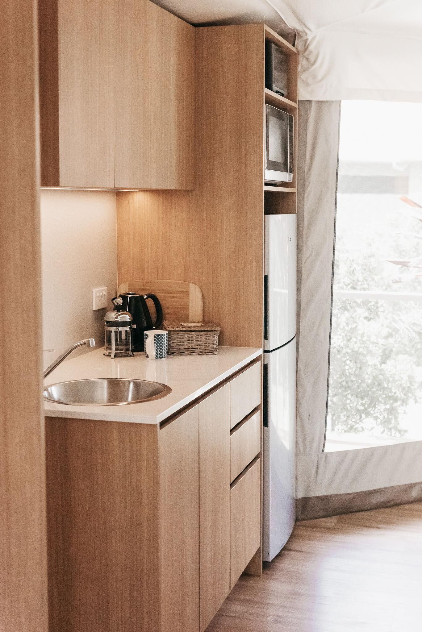 Una cocina compacta con armarios de madera, un lavamanos de acero inoxidable, un hervidor y un refrigerador.